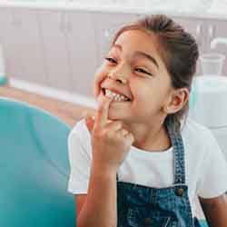 Young girl in dental chair pointing to her tooth